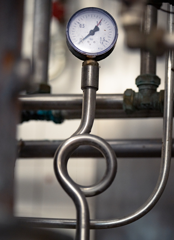 Distillerie Zimmerli Druckanzeige (in bar) angeschlossen an Röhre, im Hintergrund viele weitere Röhren
