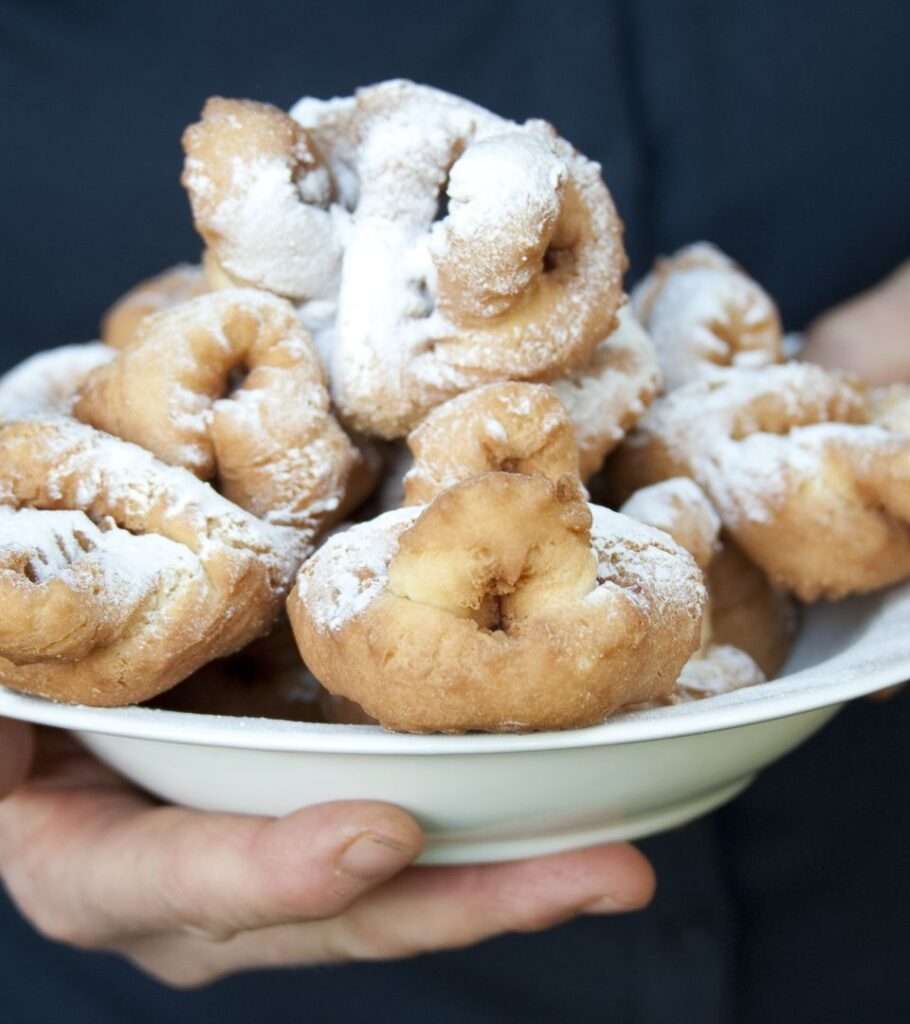 Mit Puderzucker bestreute Krapfen in einer Schüssel, die in einer Hand gehalten wird