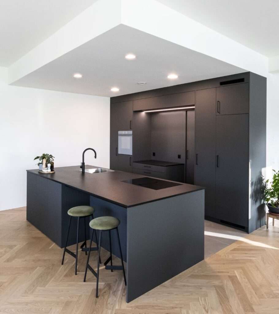 Moderne Küche mit dunkler Kücheninsel, zwei Hockern und eingebauten Geräten