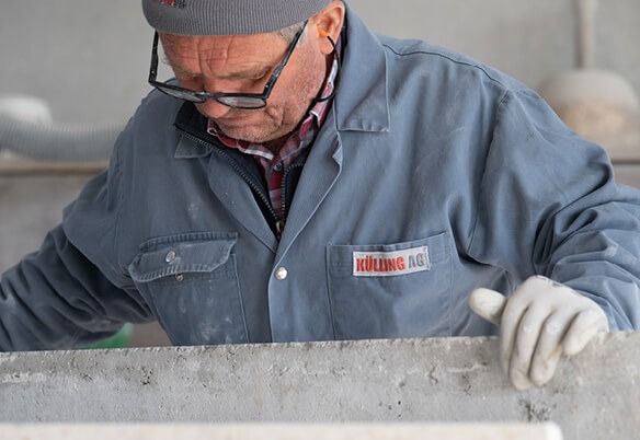 Ein Arbeiter in Schutzkleidung beugt sich über eine Betonfläche und prüft sie